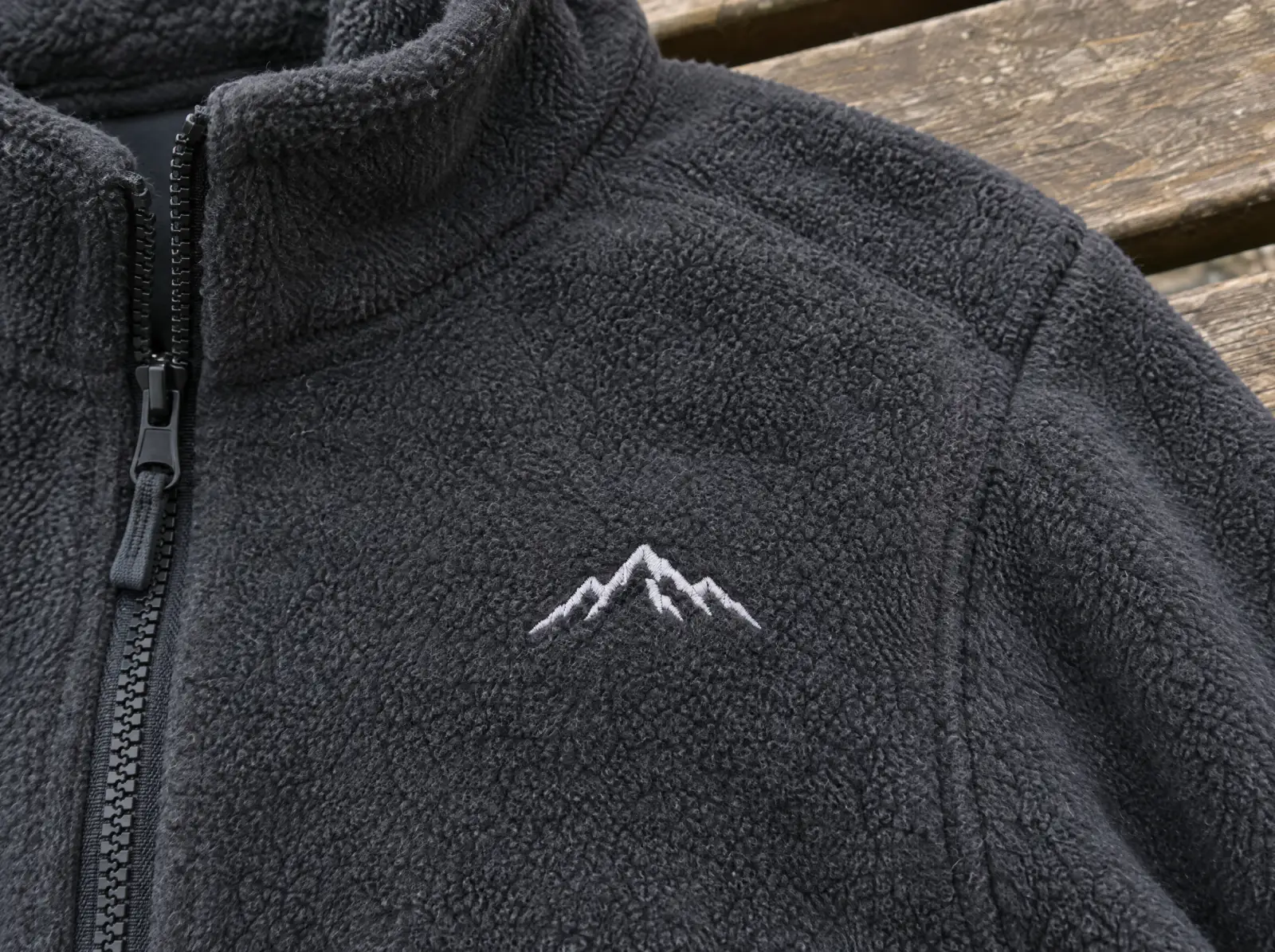 A charcoal fleece jacket with a small white embroidered mountain emblem on the chest