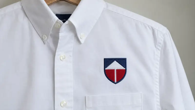 A white work shirt with an embroidered shield emblem on the chest